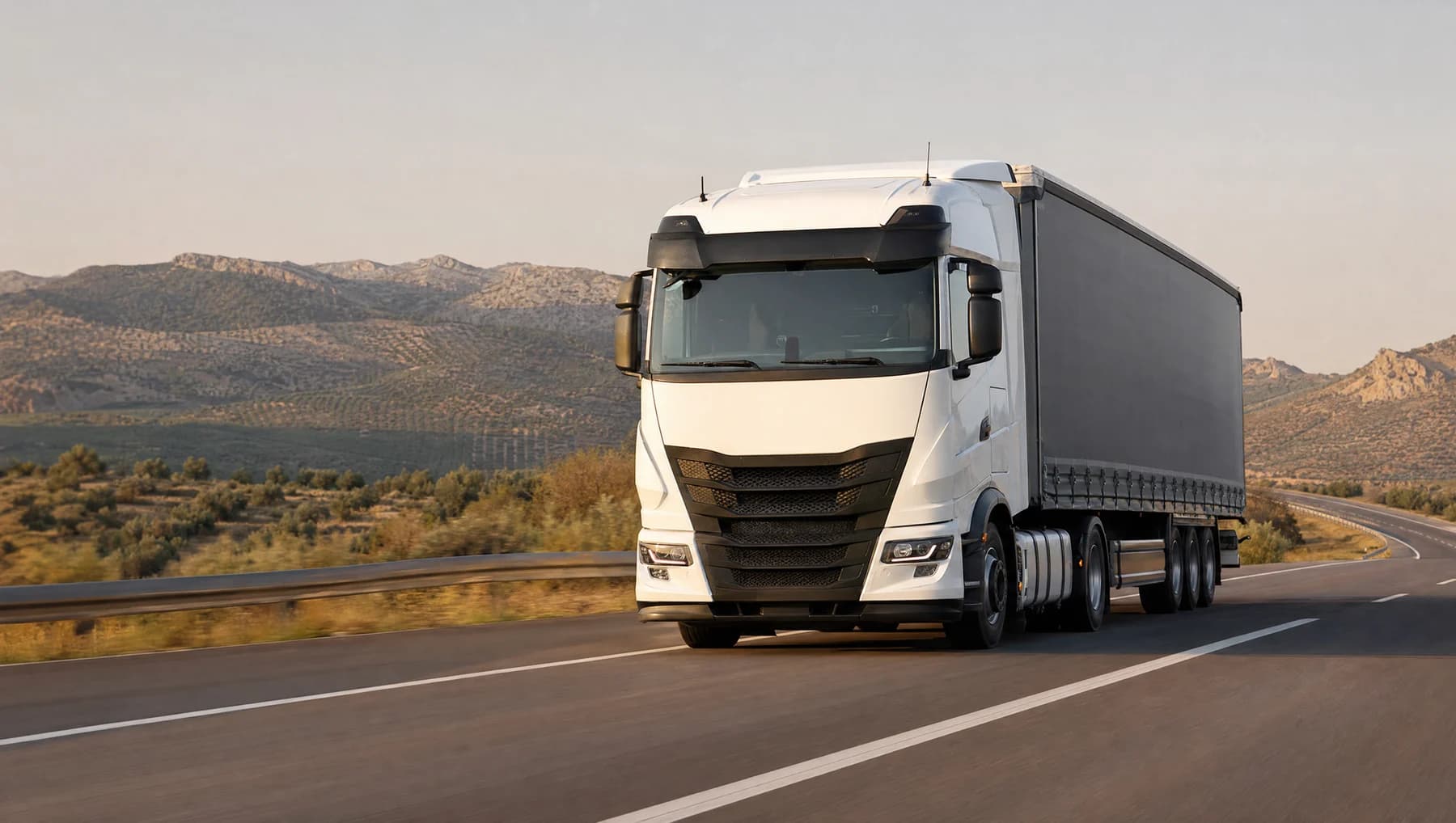 A white commercial truck on an open road through sunlit hills